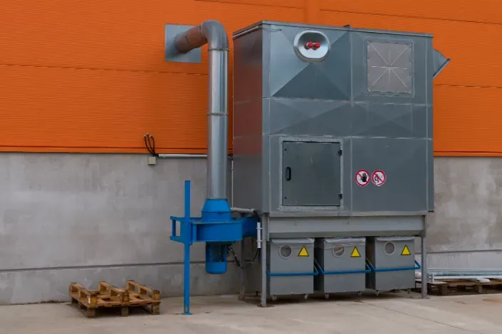 Industrial air filtration unit, gray metal, blue fan, orange building background.