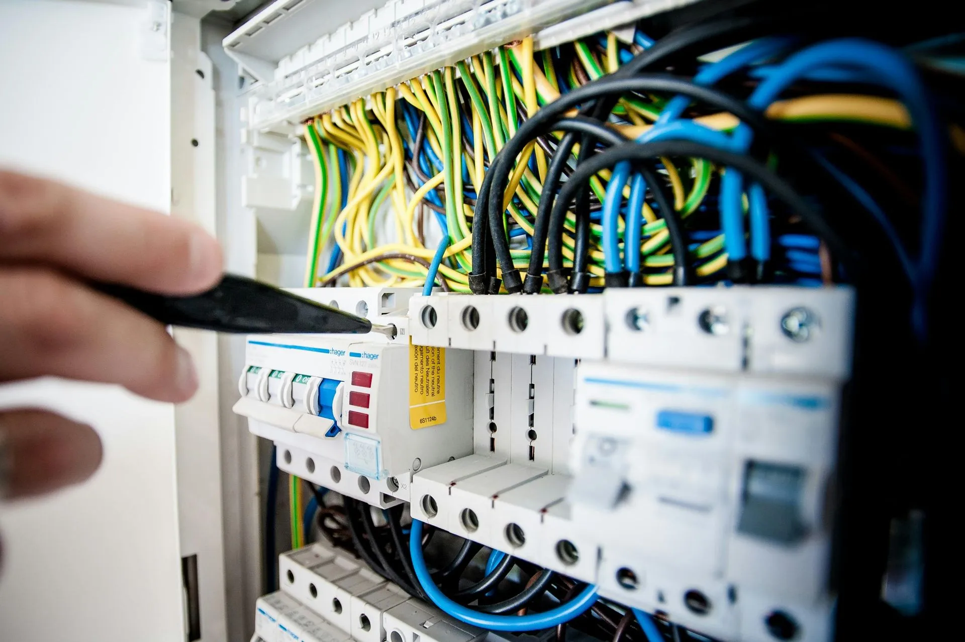 Electrician working on a circuit breaker panel, with colorful wires and safety labels.
